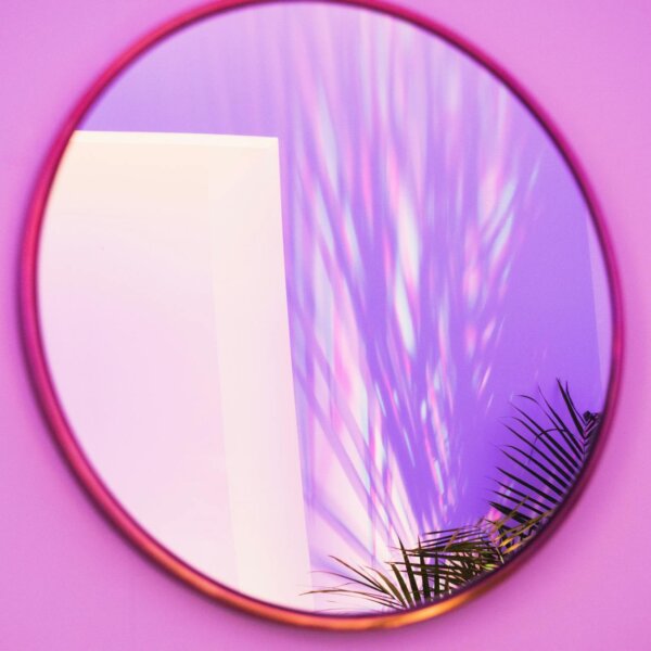 Round mirror reflecting colorful light patterns and shadow of a plant. Ideal for abstract and design themes.