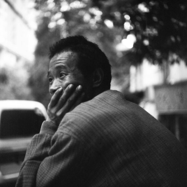 Black and white portrait of an elderly man in a contemplative pose outdoors.