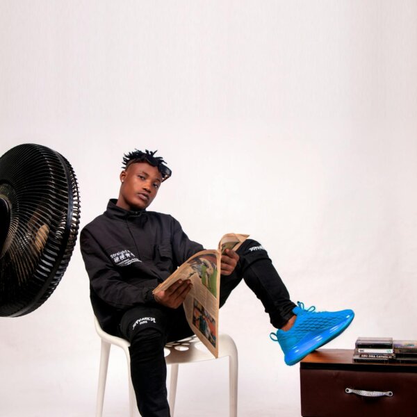 Young African man seated with newspaper, showcasing a stylish apparel in a studio setting.