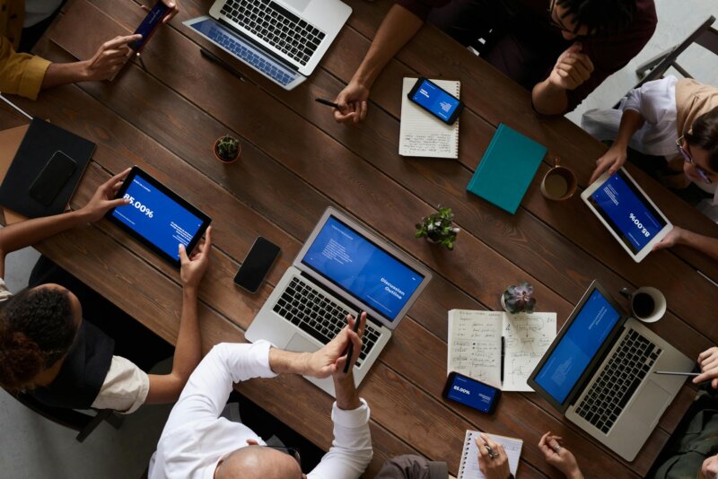 Overhead view of a diverse team discussing around a wooden table, using technology.